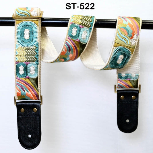 A colorful, patterned guitar strap with a floral design, hanging on a black metal bar.