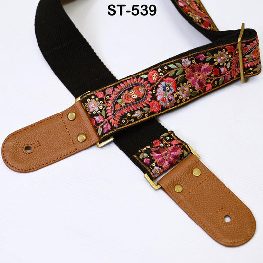A colorful, patterned guitar strap with a black leather buckle and gold hardware.