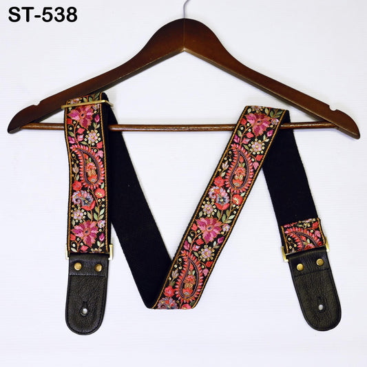 A pair of black guitar straps with a floral pattern and gold accents, hanging on a wooden hanger.