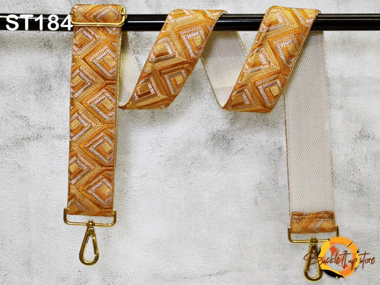 a gold-colored strap with a geometric pattern, hanging on a black bar.