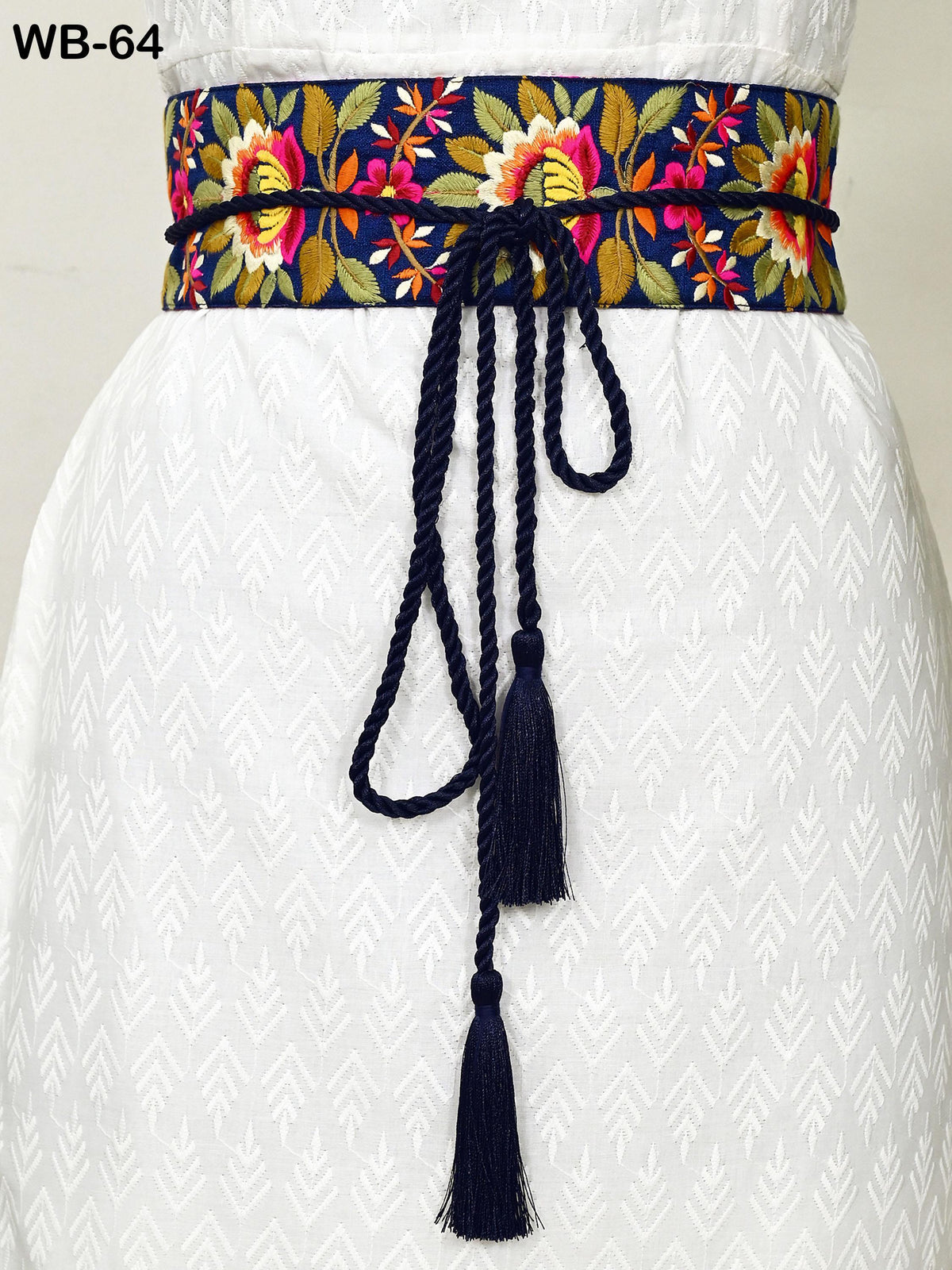 a close-up view of a white dress with a decorative belt featuring a floral pattern and tassels.
