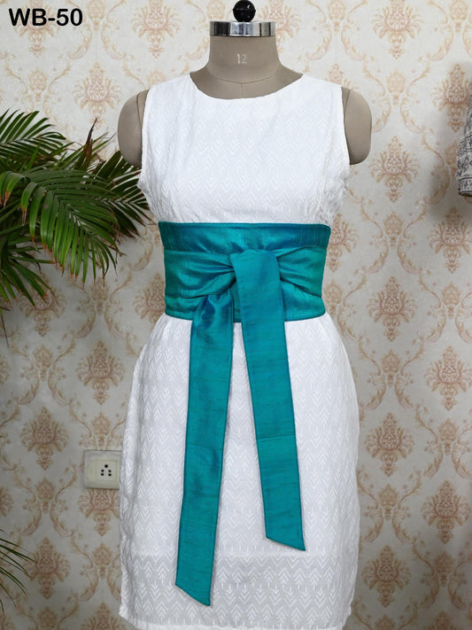 A mannequin wearing a white dress with a turquoise sash, displayed against a patterned wallpaper.