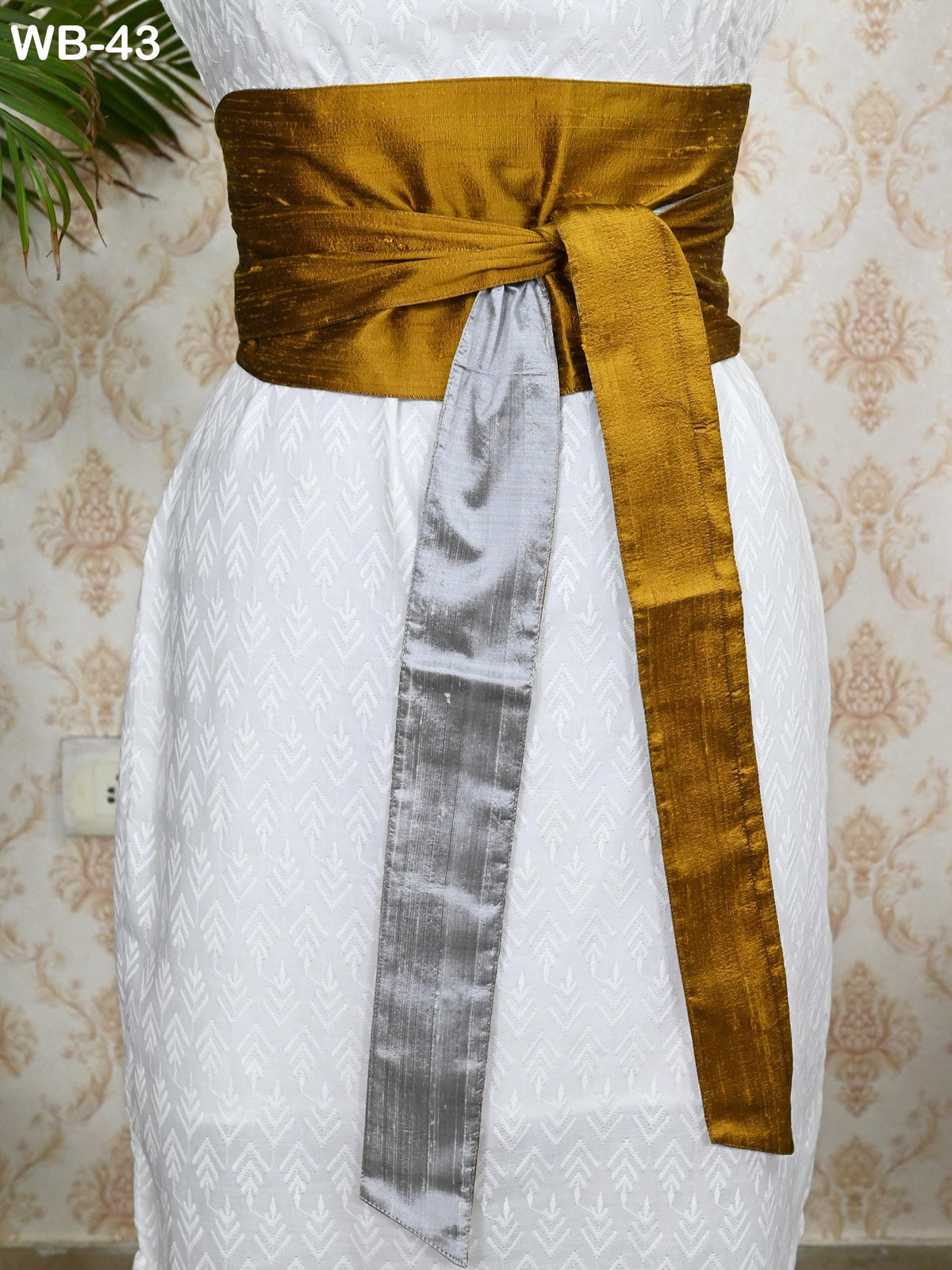 a person wearing a white dress with a gold and silver sash tied around the waist.