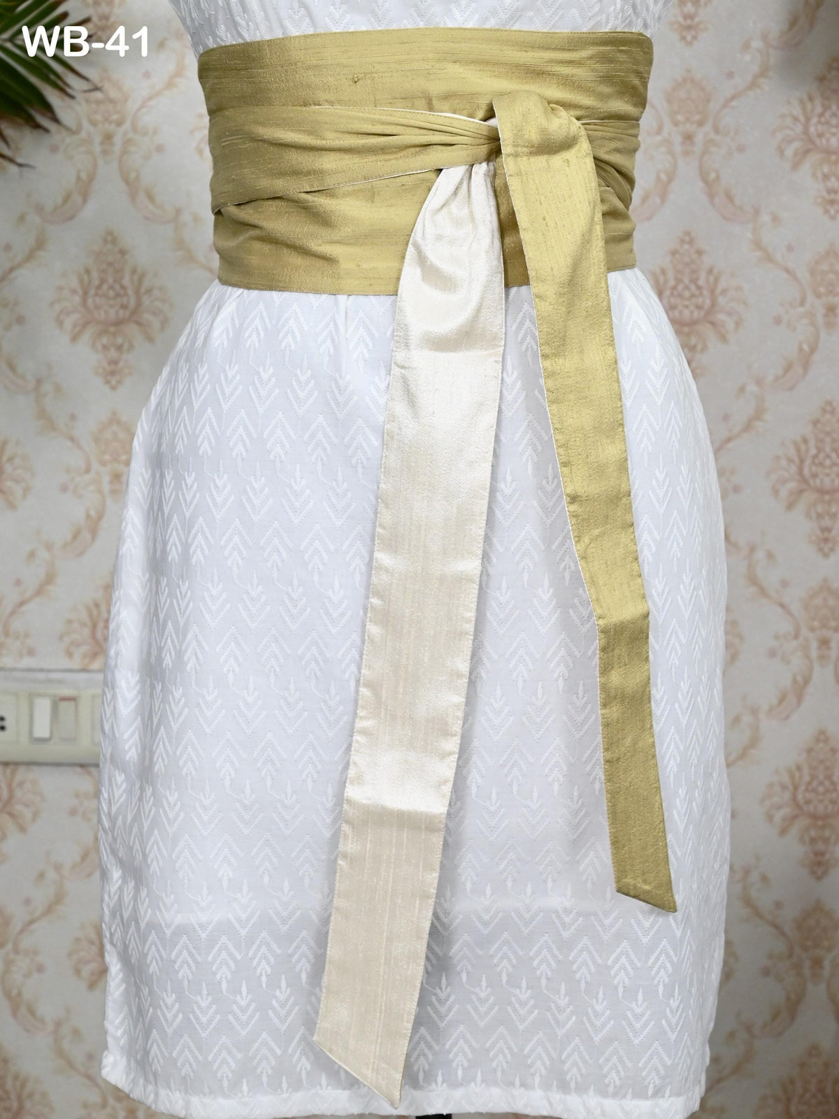 A mannequin wearing a white dress with a gold sash tied around the waist.