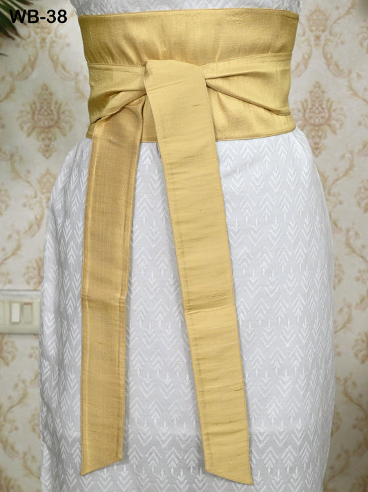 a gold belt tied around a white dress with a patterned design.