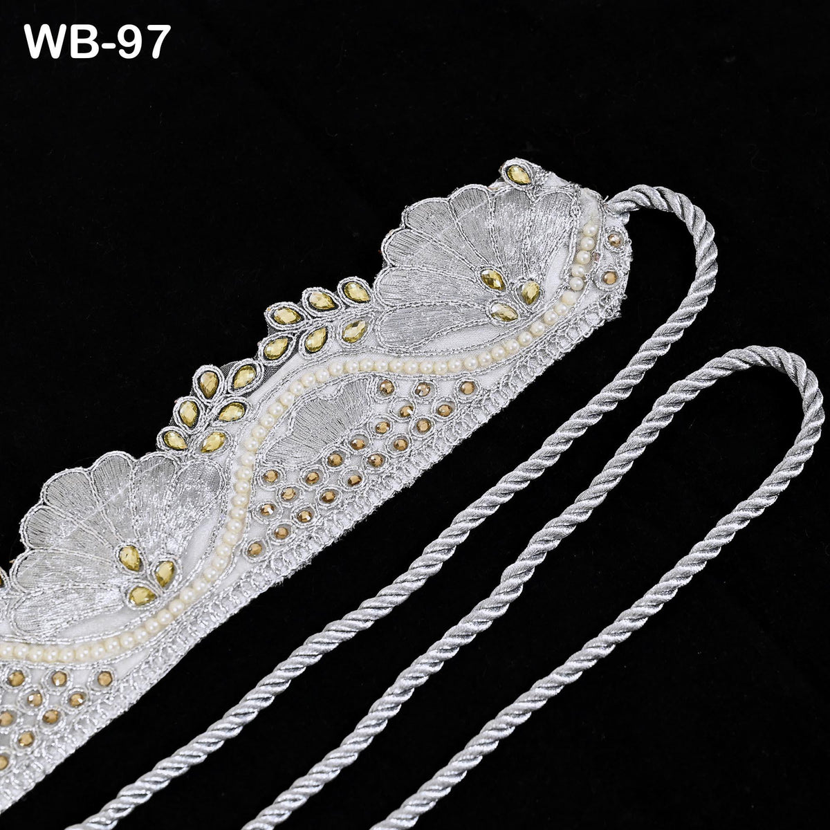 a decorative piece of jewelry, possibly a necklace or bracelet, with intricate silver and gold embroidery and pearls. The piece is displayed against a black background, highlighting its elegant design.