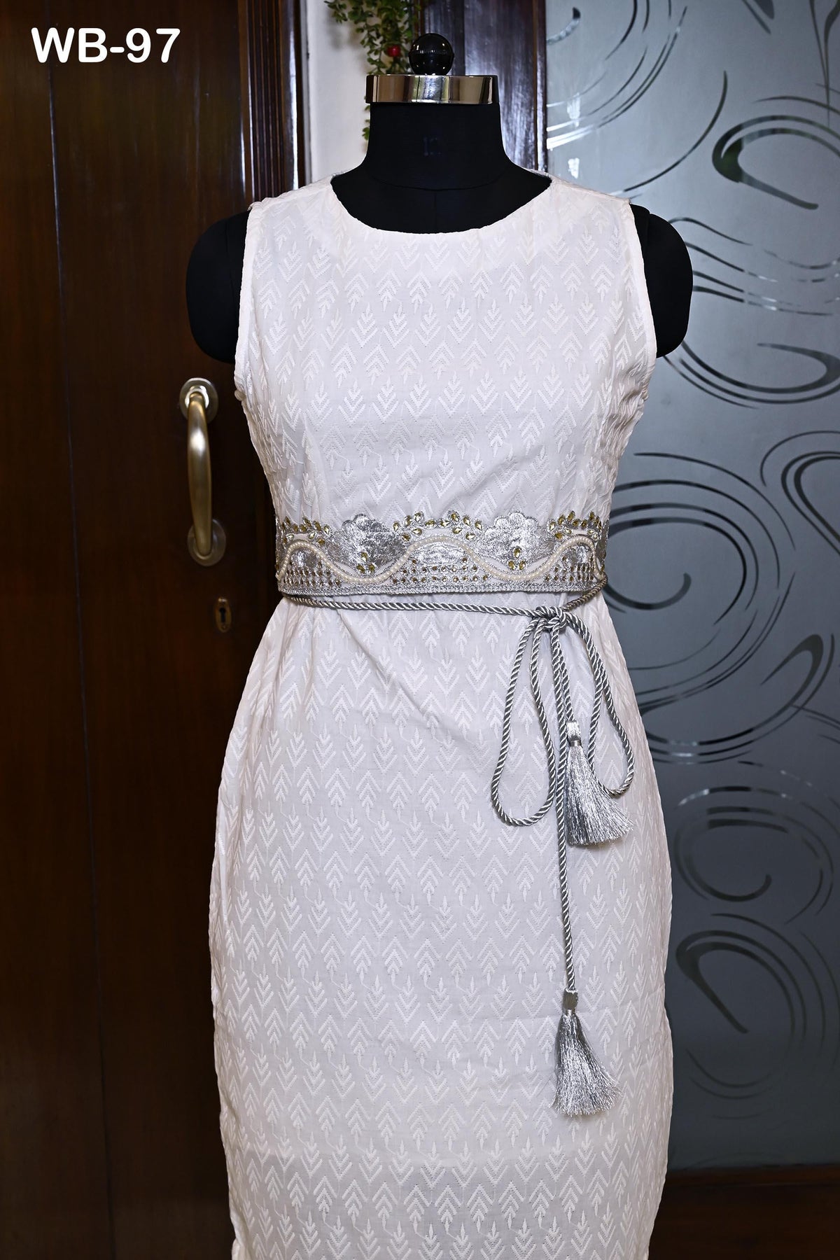 A white dress with a silver belt and tassel is displayed on a mannequin.