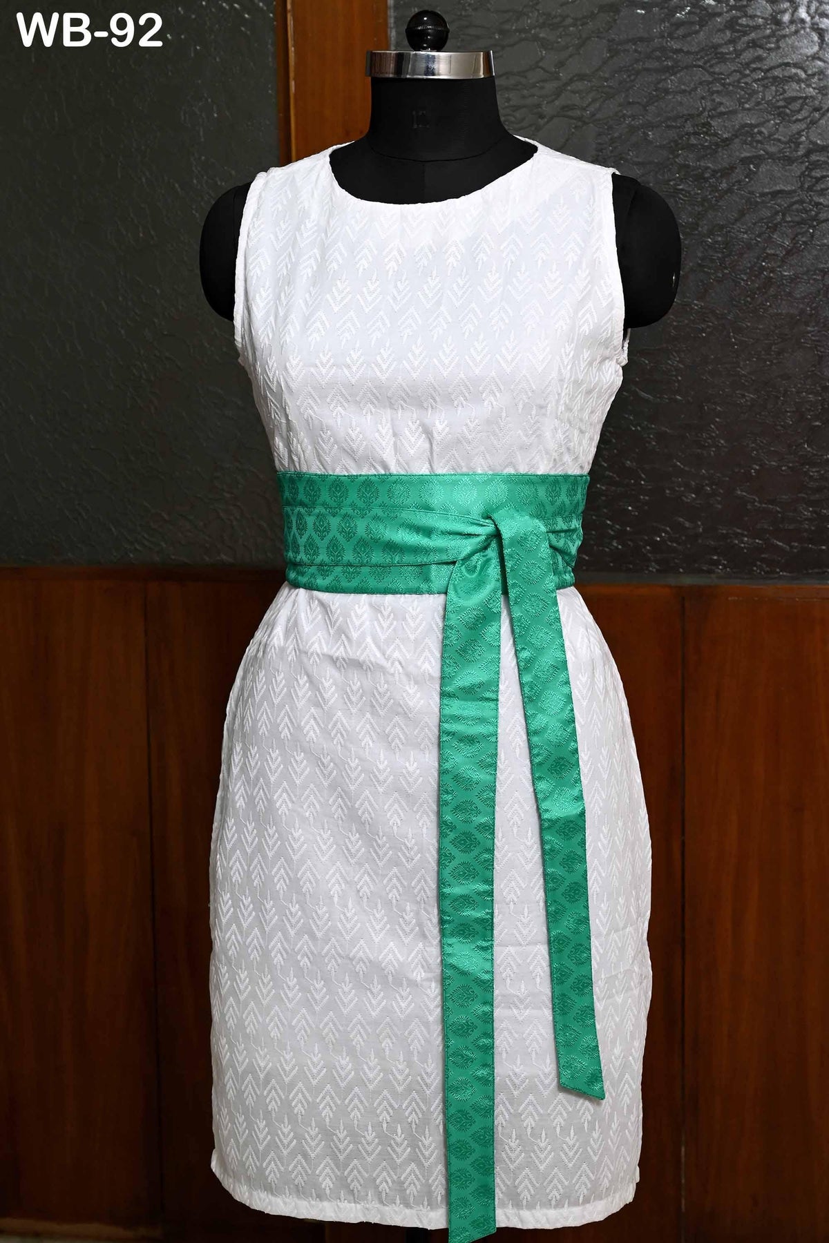A white dress with a green sash, displayed on a mannequin.