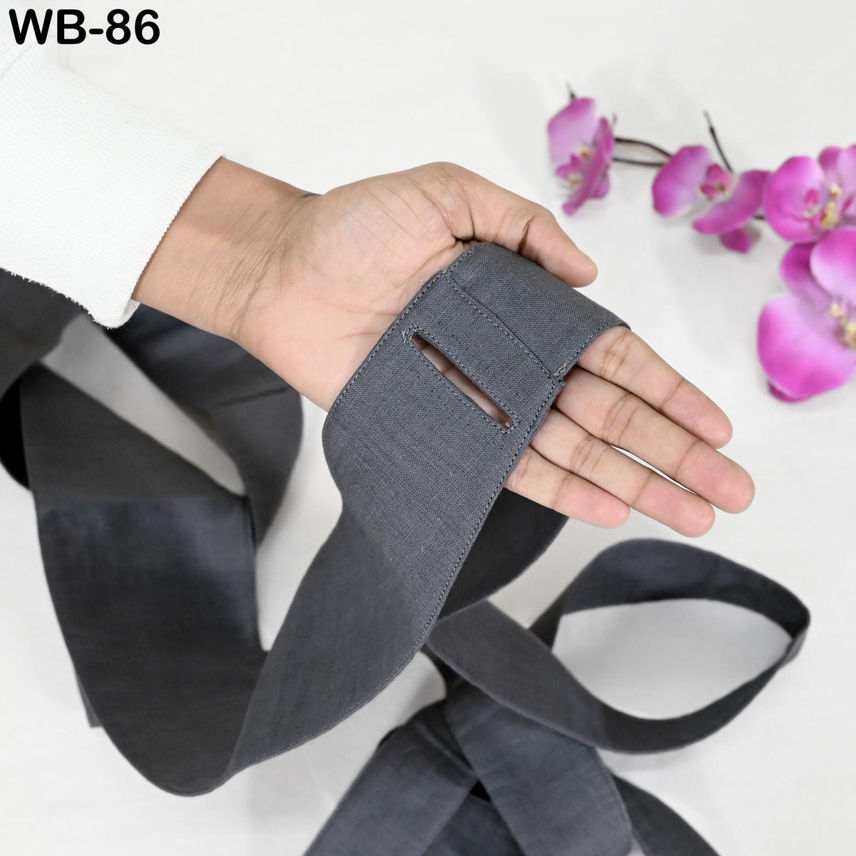 A hand is holding a gray fabric with a small cut in it, and there are pink orchids in the background.