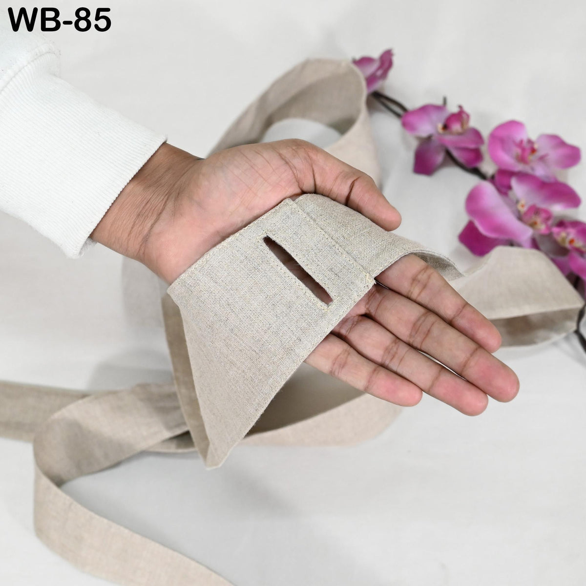 A hand is holding a beige fabric with a cutout in it, positioned next to a bunch of pink flowers.