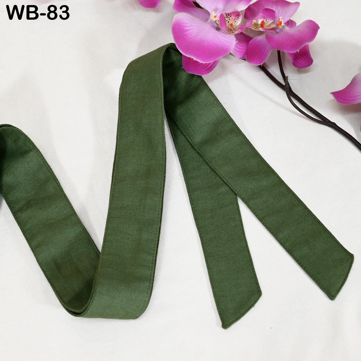 a green ribbon or band lying on a white surface, with a branch of pink orchids or flowers in the background.