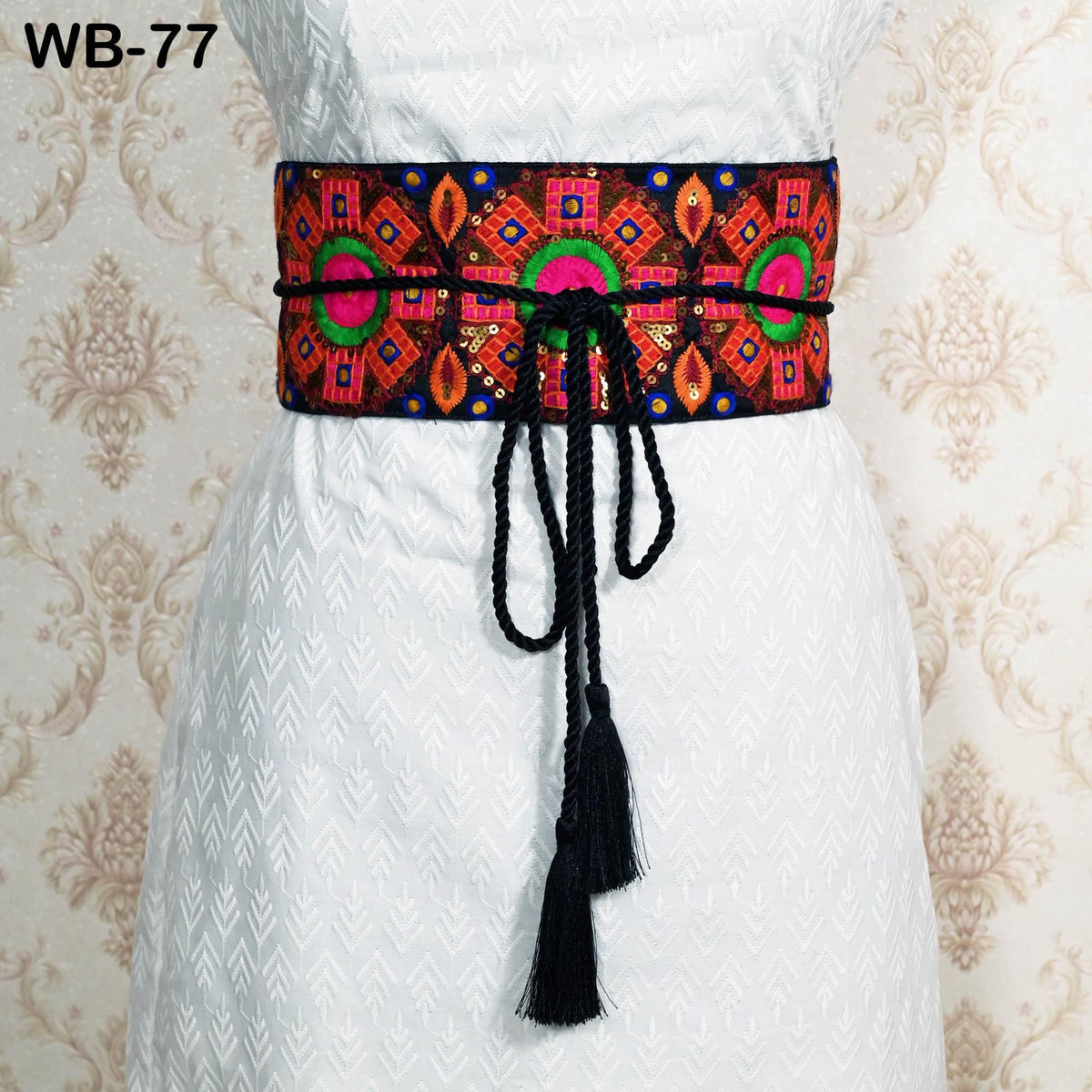 A white dress with a colorful, patterned belt featuring a tassel.
