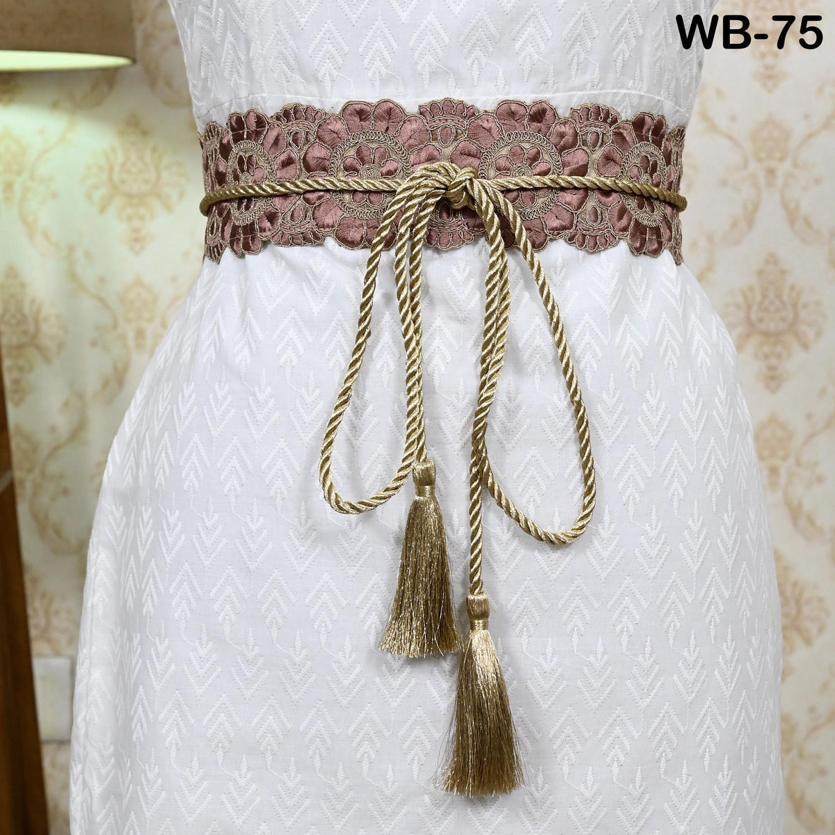 A close-up view of a white dress with a decorative belt featuring a floral pattern and tassels.