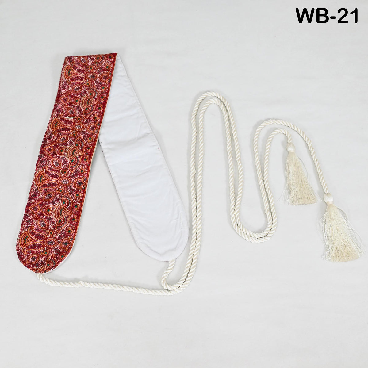 a red and white paisley-patterned scarf with a white tassel attached, lying on a white surface.