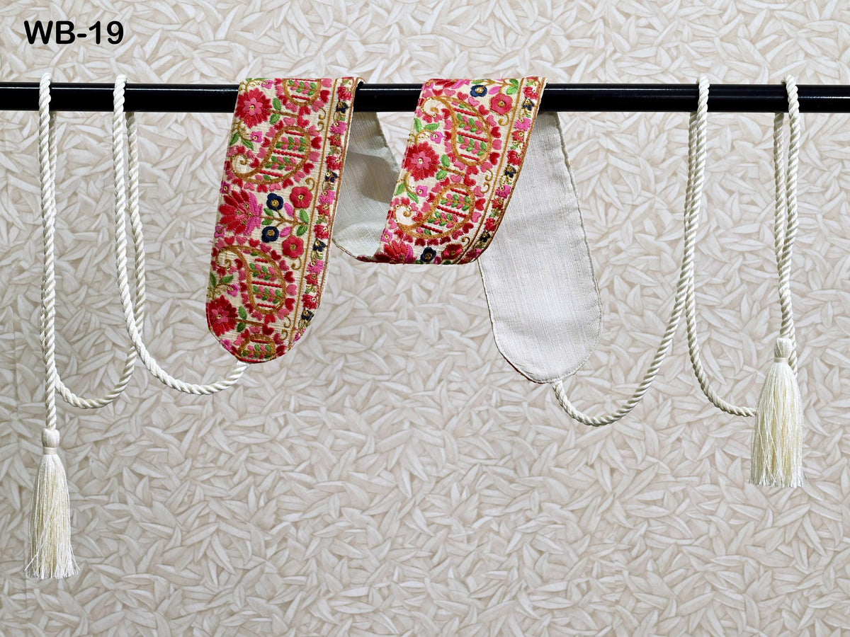 a pair of decorative fabric earrings hanging on a black bar, with white tassels attached to the ends of the earrings.