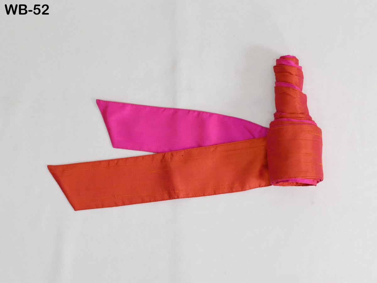 a pink and orange ribbon or fabric item, possibly a decorative piece or accessory, lying on a white surface.