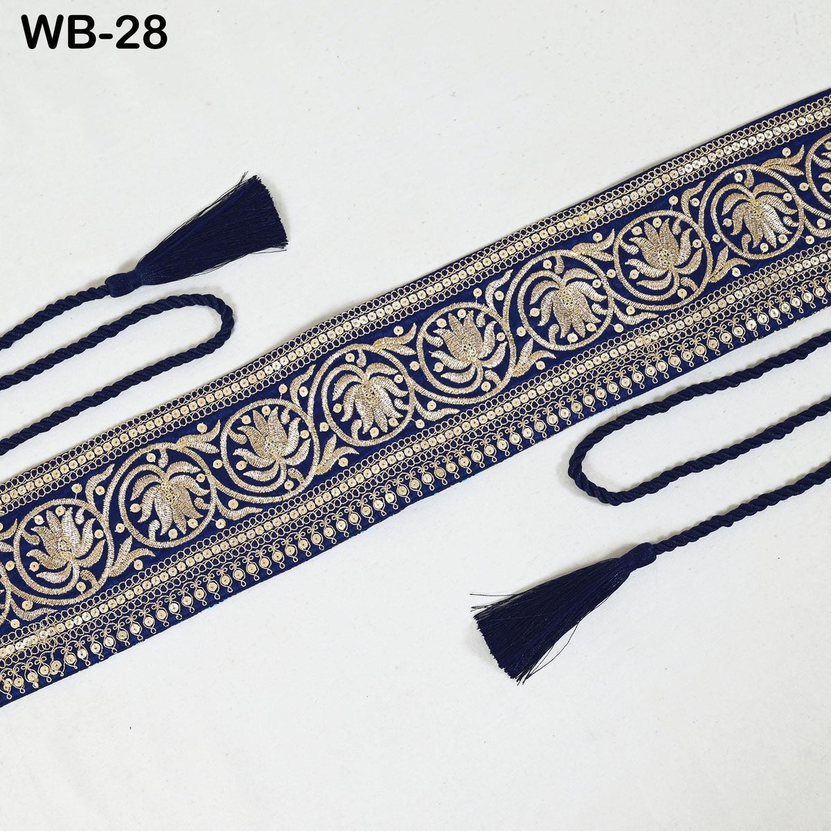 a decorative blue and gold embroidered fabric with a repeating floral pattern. The fabric has a tassel attached to the ends, and there are two tassels visible on the right side of the image.