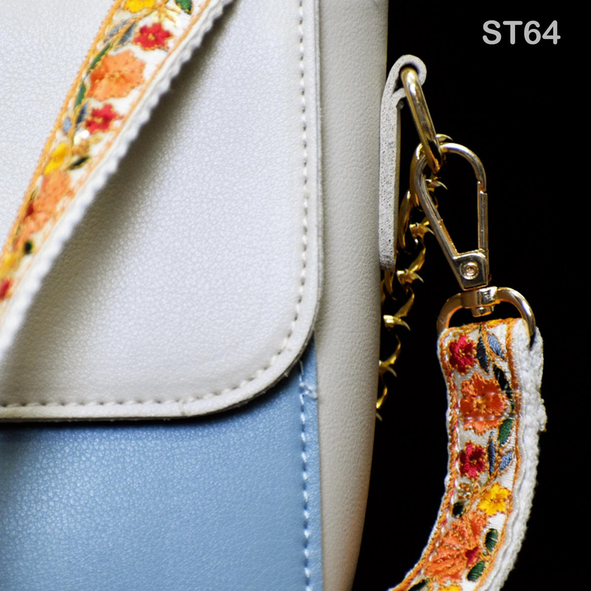 A close-up view of a white and blue handbag with a floral pattern on the strap and a gold-colored metal clasp.
