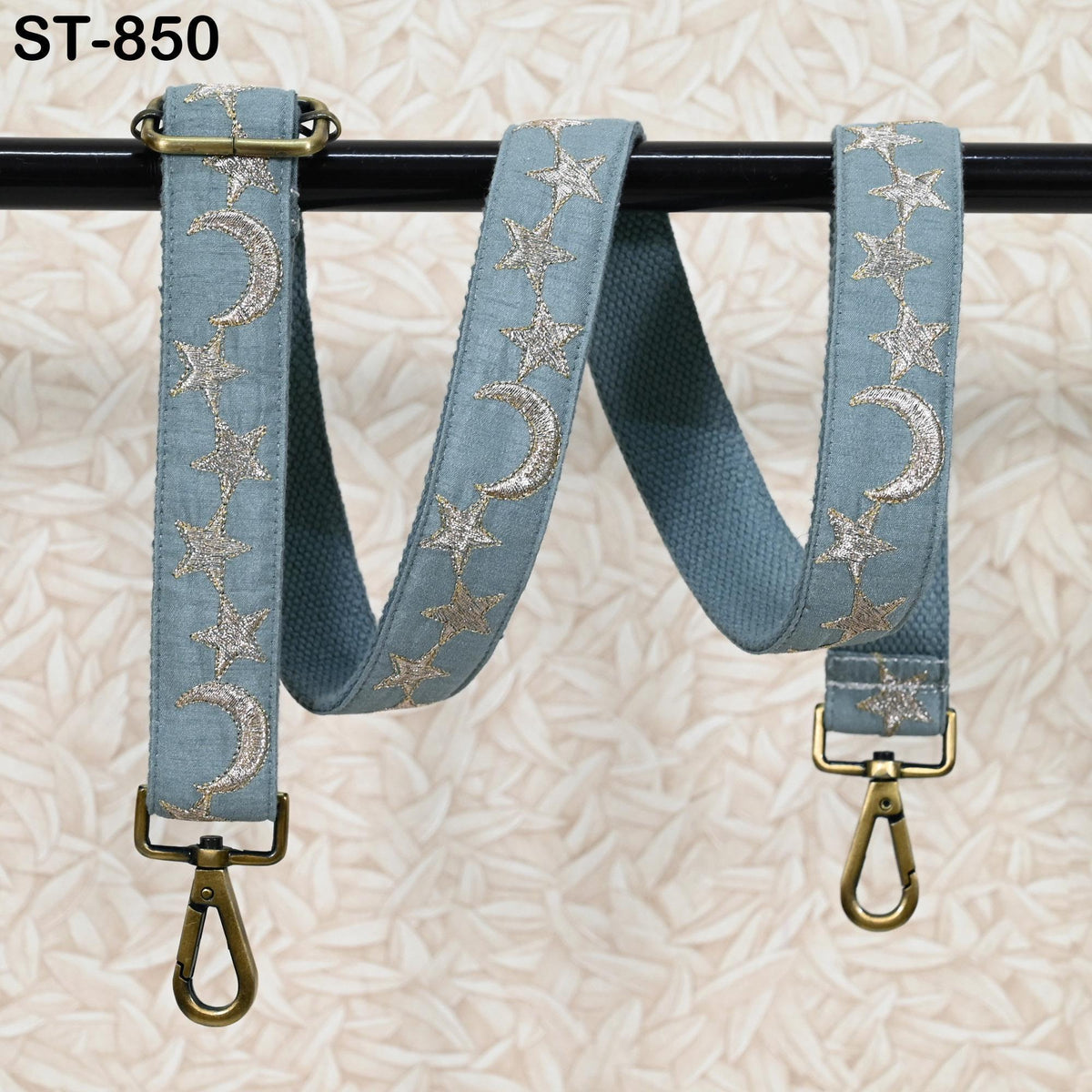 A pair of blue star and crescent-patterned straps with metal buckles, hanging from a black metal bar.