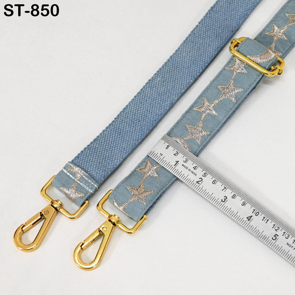 a blue strap with gold-colored metal hooks and a ruler placed on a white surface.