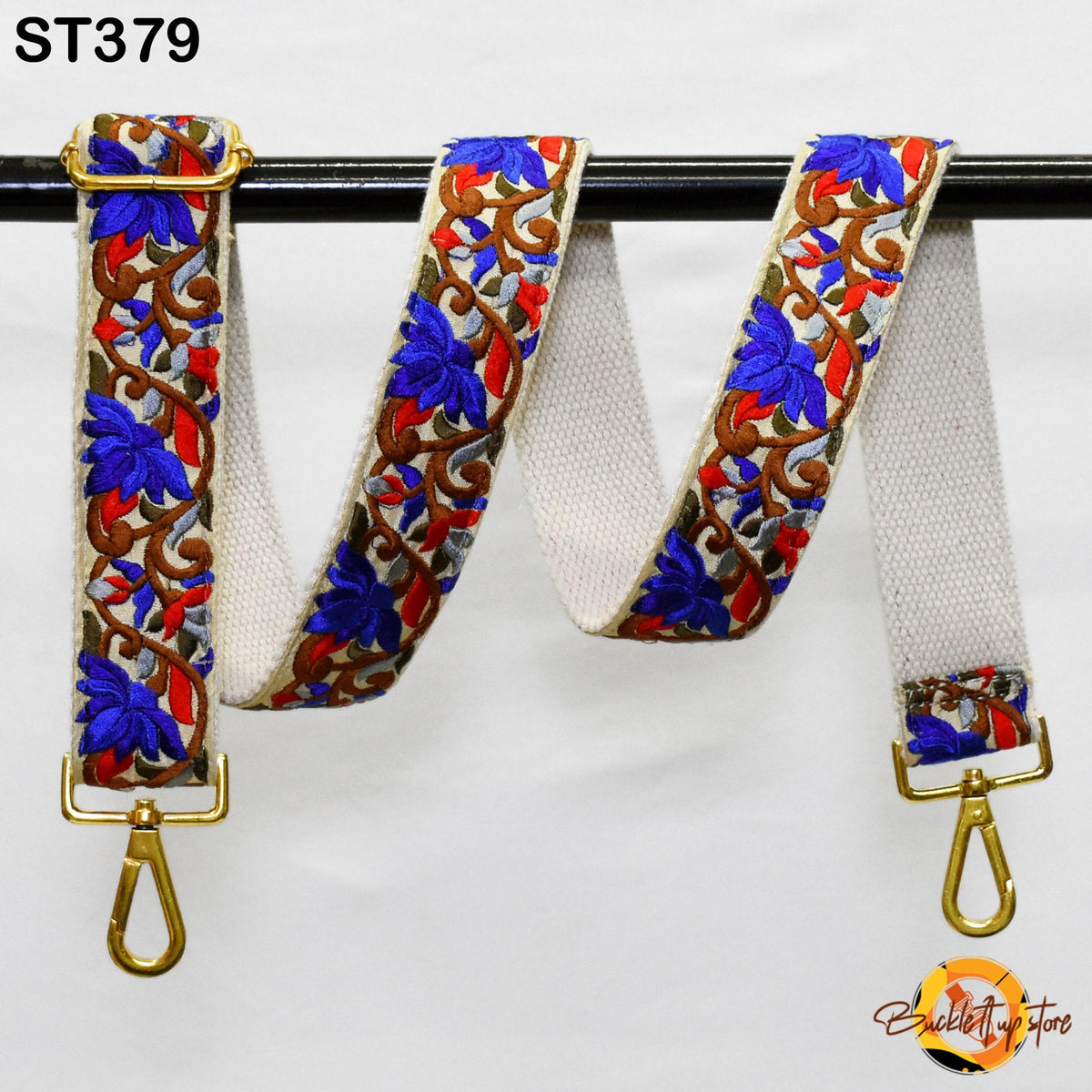 A colorful, embroidered strap with a gold metal buckle, hanging on a black rod.