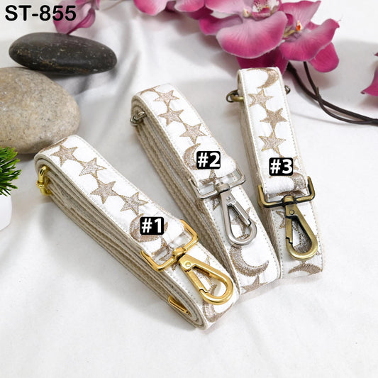 Three white straps with gold star patterns, each with a metal clasp, are displayed on a white surface.