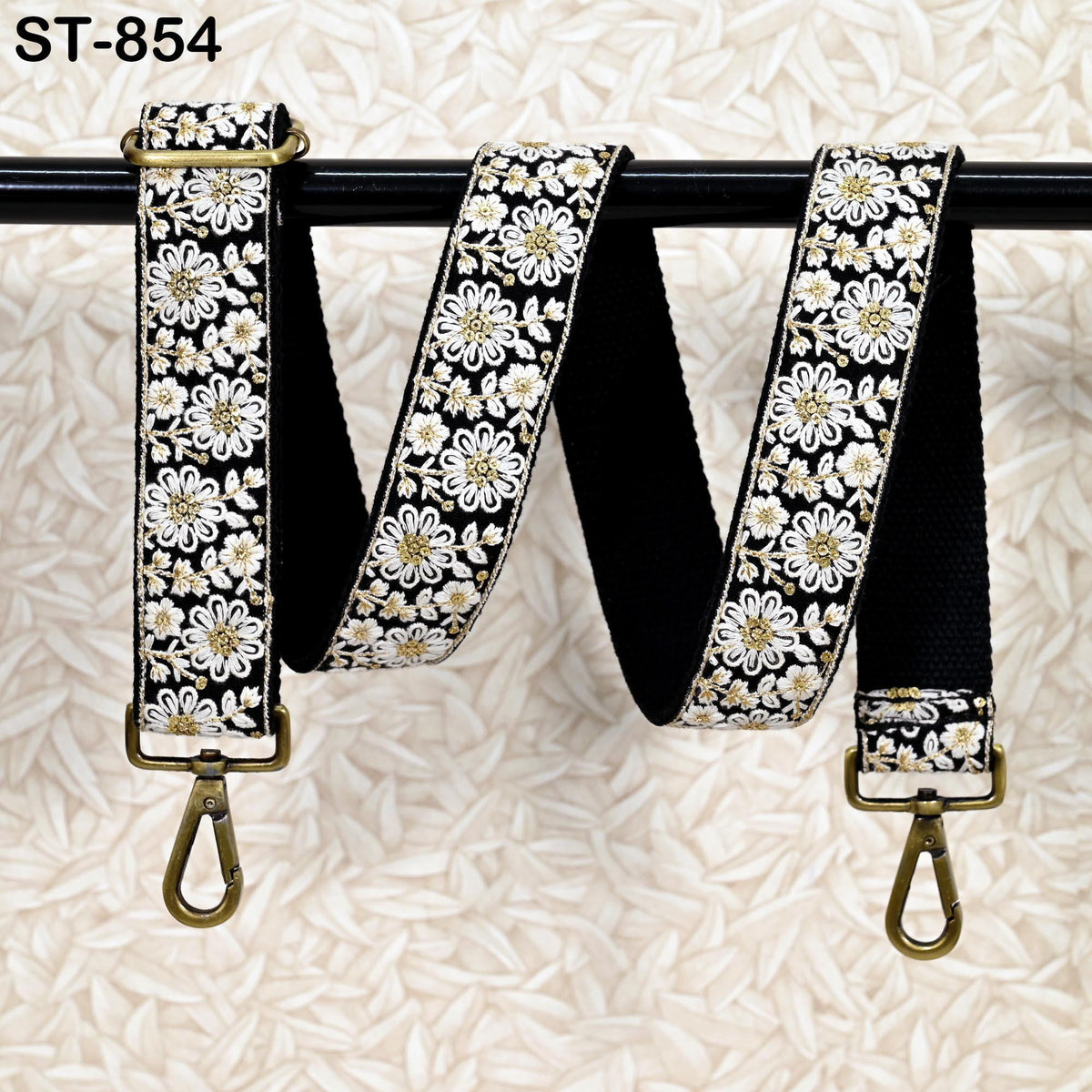 A floral-patterned black and white strap with gold accents, hanging on a black rod.