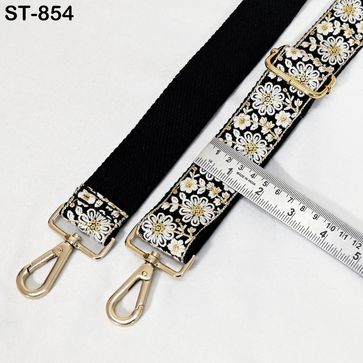 A black strap with a floral pattern and two metal hooks, accompanied by a ruler for size comparison.