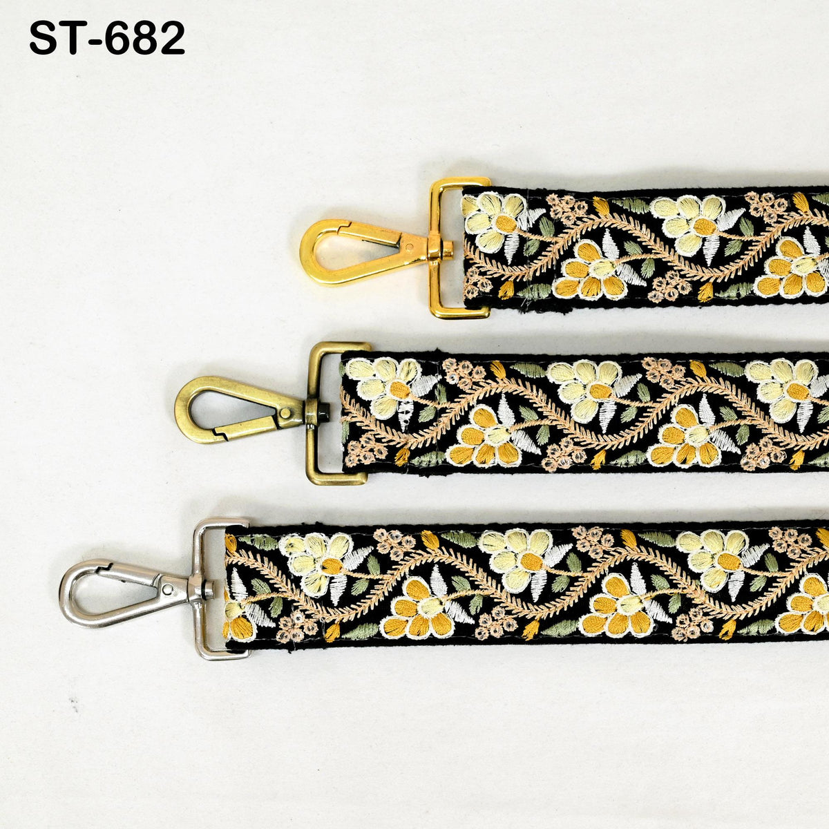 three straps with floral embroidery, each with a metal clasp and hook. The straps appear to be made of black fabric with gold and white floral patterns.