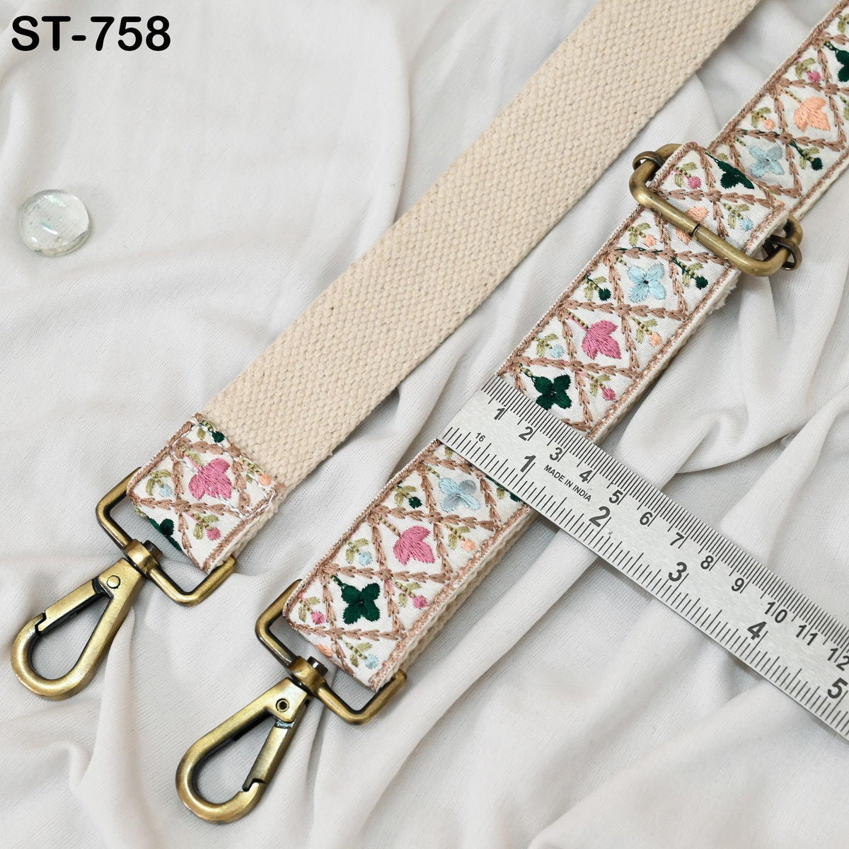 a beige strap with a floral pattern, a metal clasp, and a ruler for size comparison.
