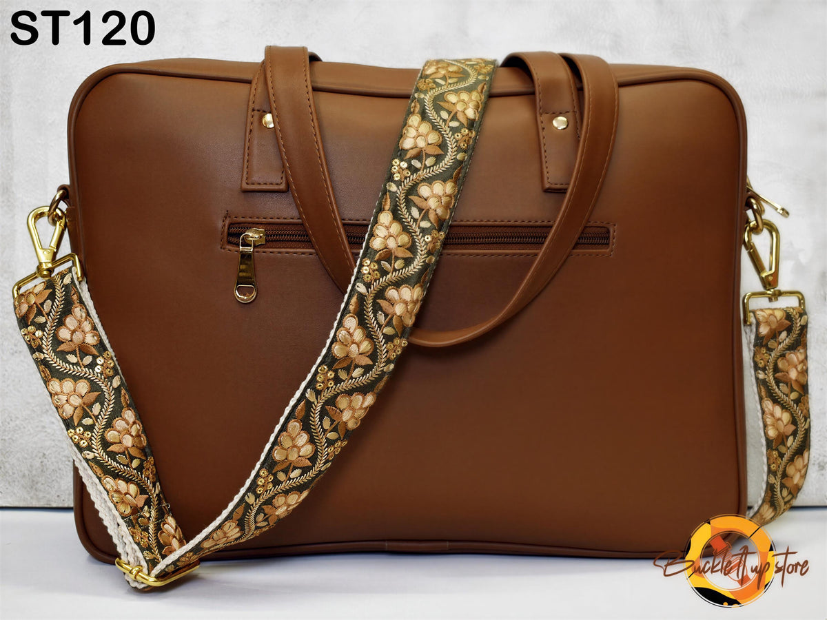 A brown leather laptop bag with a floral patterned strap, featuring a zipper closure and two gold-colored metal buckles.