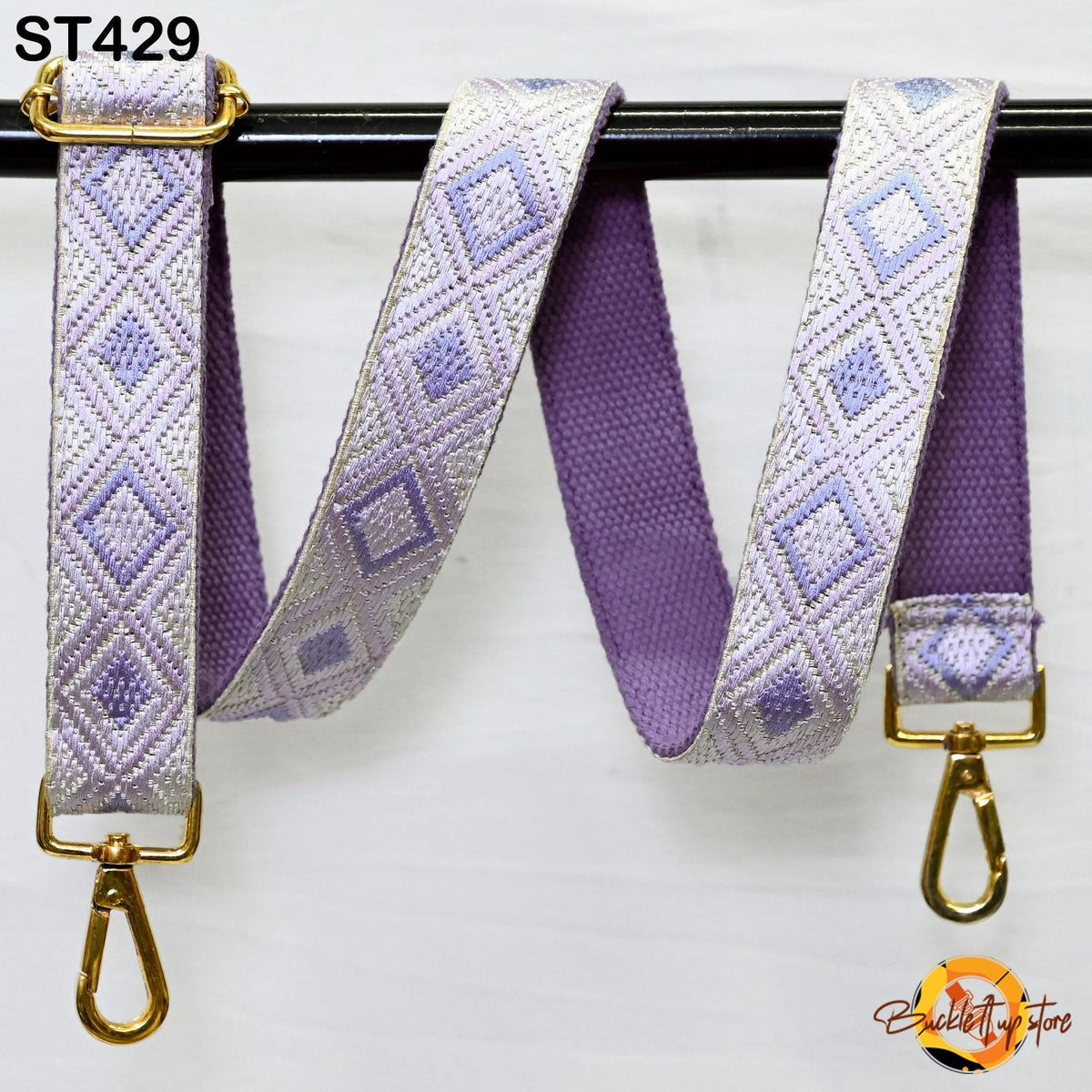 a purple and white patterned strap with a gold metal buckle, hanging on a black bar.