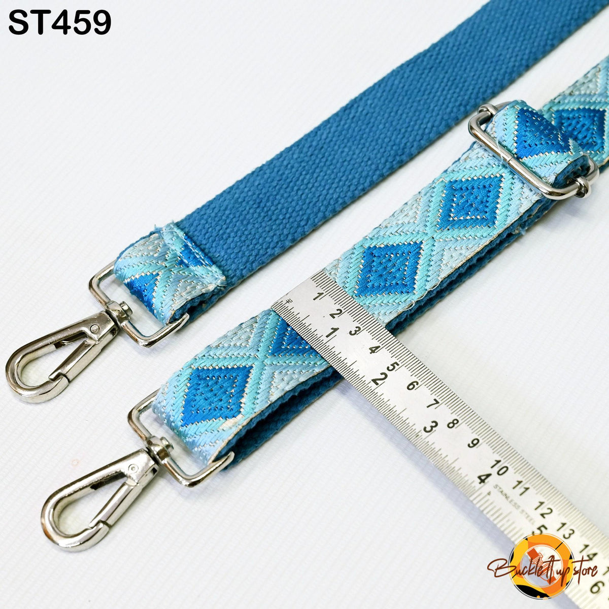a blue and white patterned strap with metal hooks, and a ruler is placed next to it, indicating the strap's length.