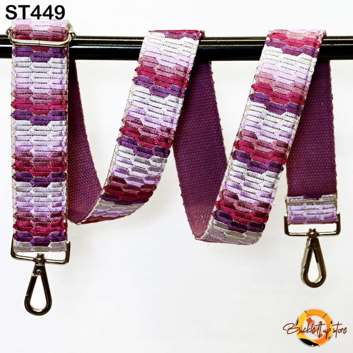 A colorful, patterned strap with a metallic hook attached, hanging on a black bar.