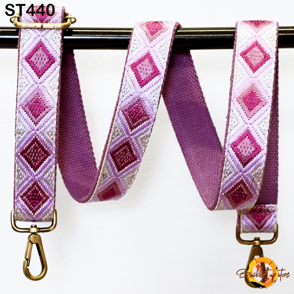 a pink and white patterned strap with a metal clasp and hook attached to a black metal bar.