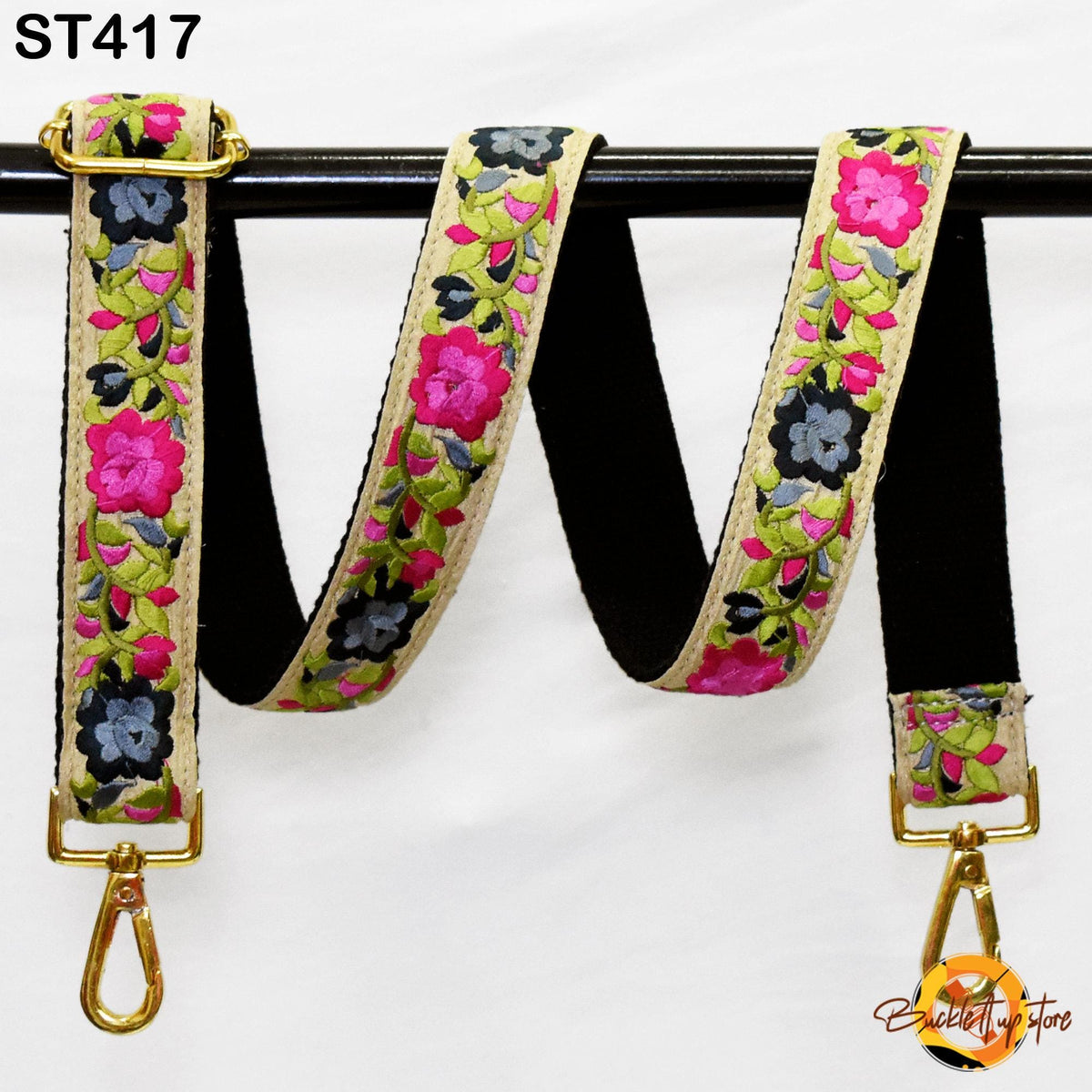A floral-patterned black and gold strap with a gold buckle, hanging on a black rod.