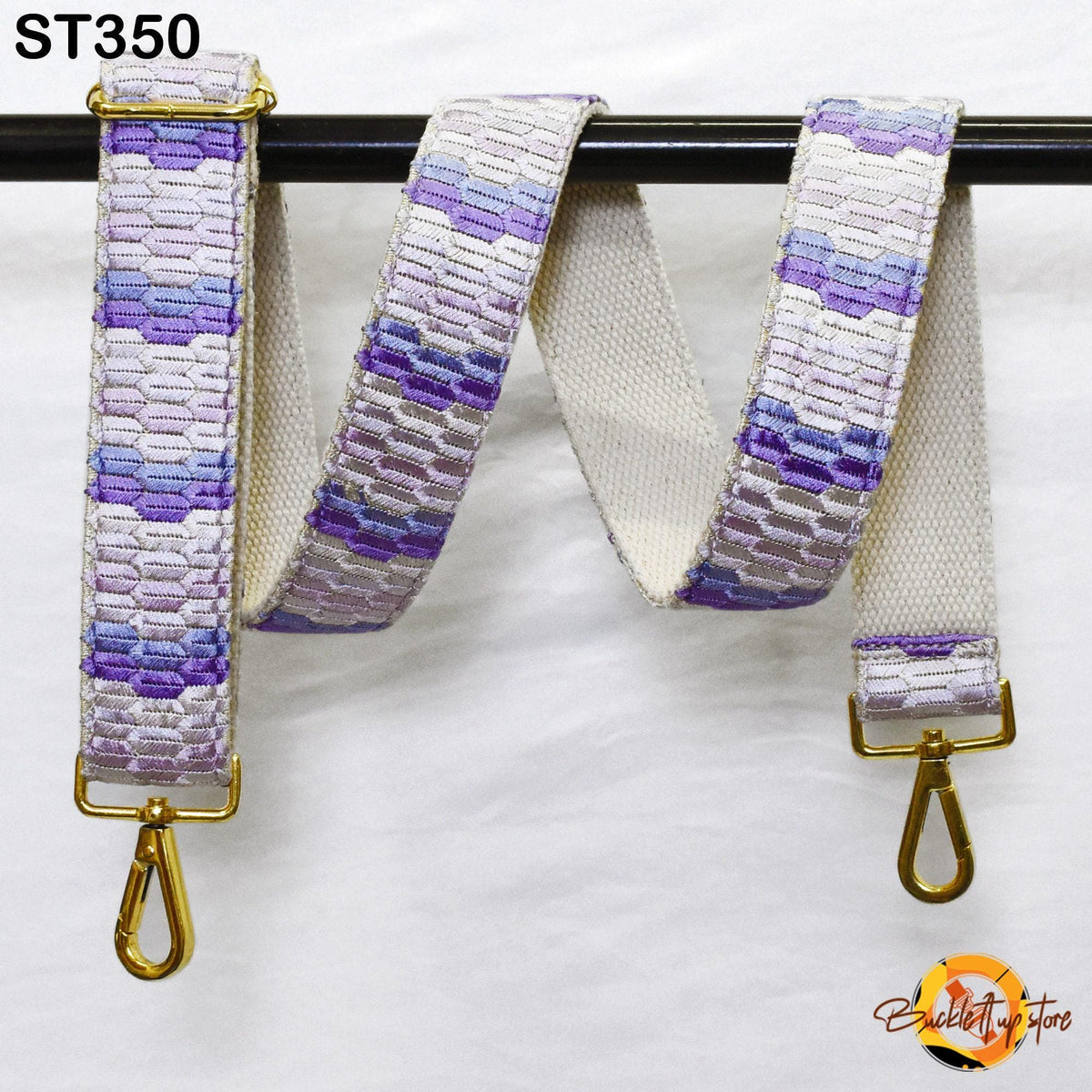 a colorful strap with a pattern of purple and white hues, hanging from a black bar.