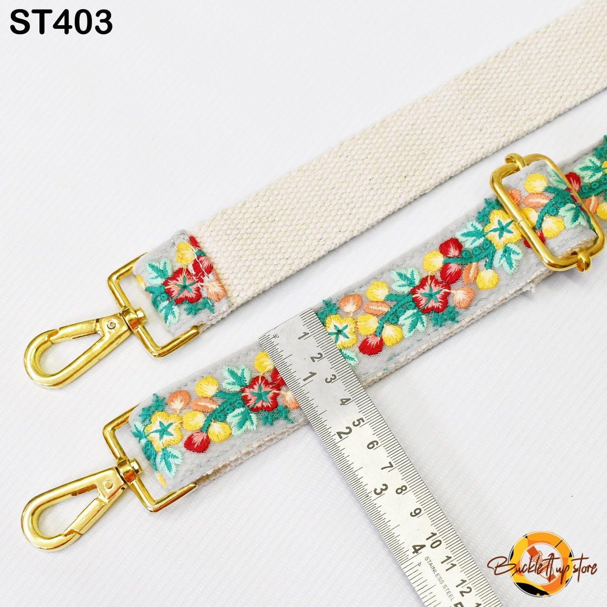 a white strap with a floral embroidered pattern, and a ruler is placed next to it, indicating the strap's length.