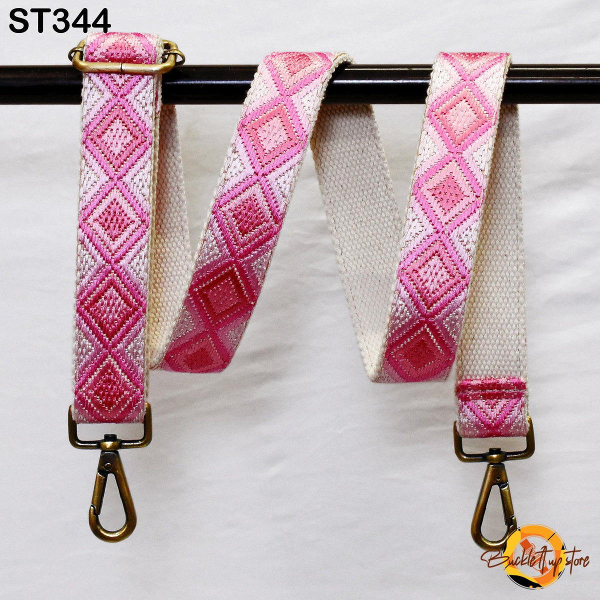 a pink and white patterned strap with a metal clasp and hook attached to a black metal bar.