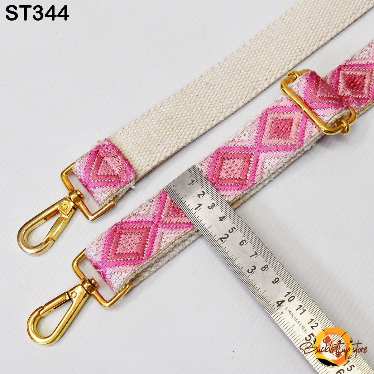 a strap with a pink and white diamond pattern, and a ruler is placed next to it, indicating the strap's length.
