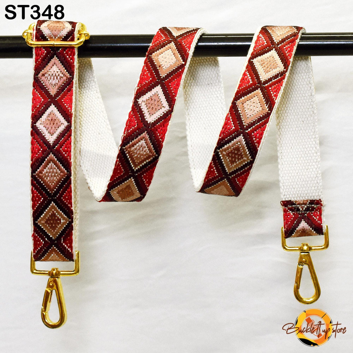 A colorful, patterned strap with a gold metal buckle attached to a black metal bar.
