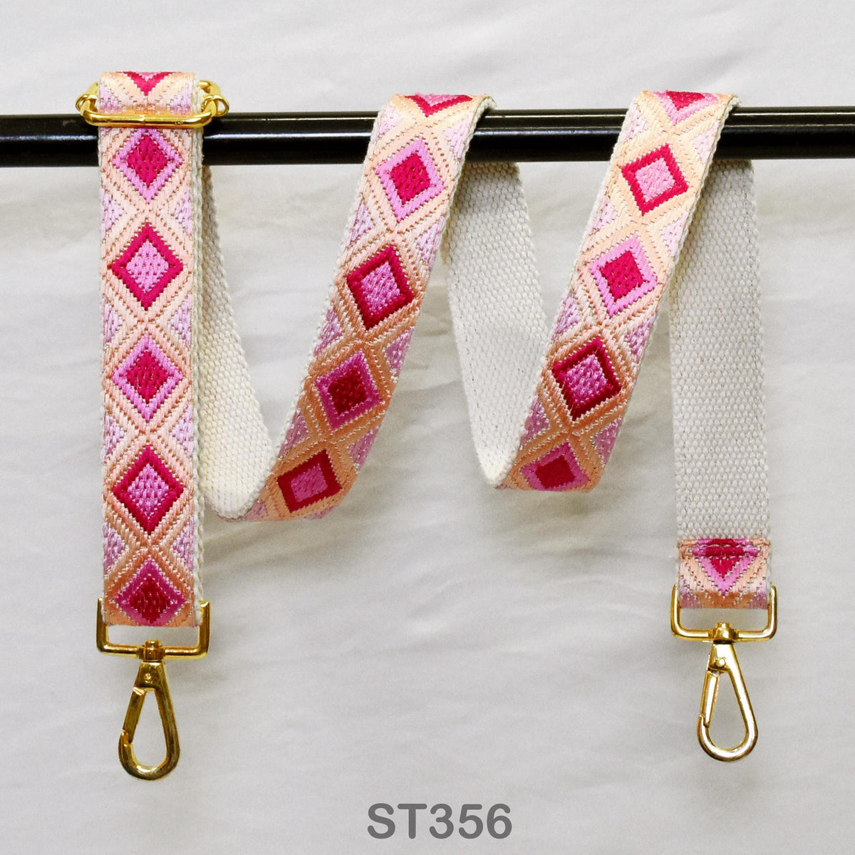 A pair of colorful, patterned straps with gold buckles, hanging on a black rod.