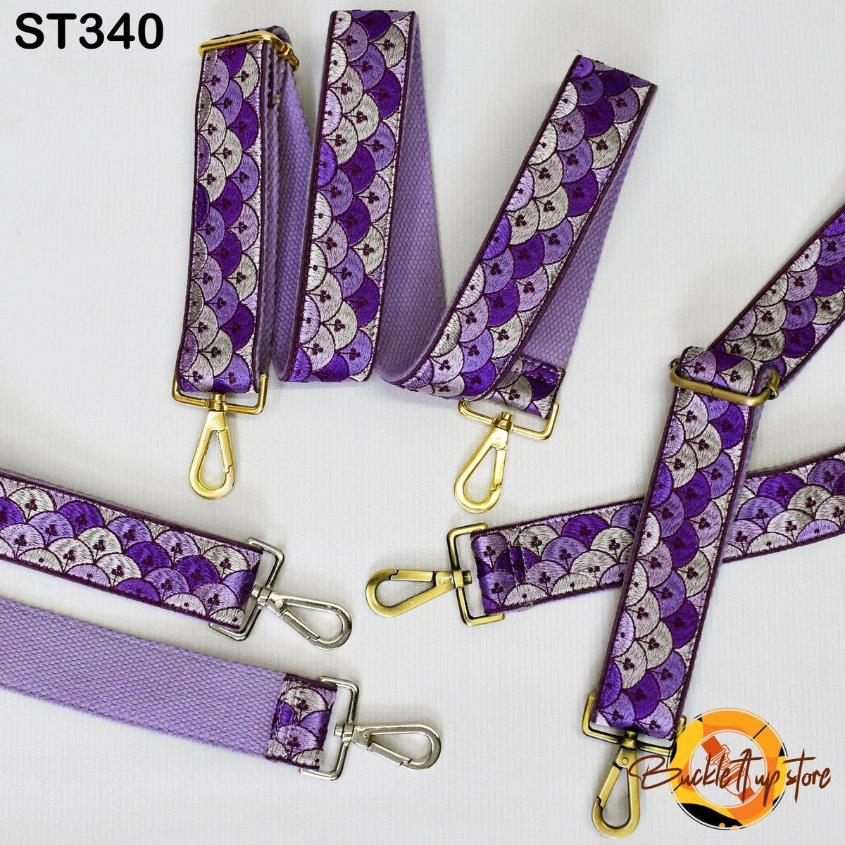a collection of purple and white patterned straps with gold metal hardware, including straps and hooks, arranged on a white background.