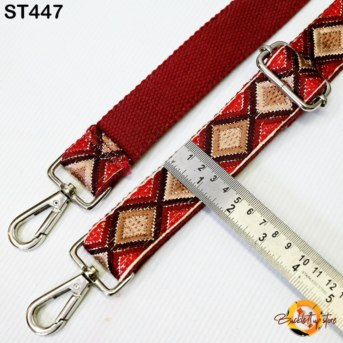 a red and brown patterned strap with a metal clasp and a ruler placed next to it, indicating the strap's size.