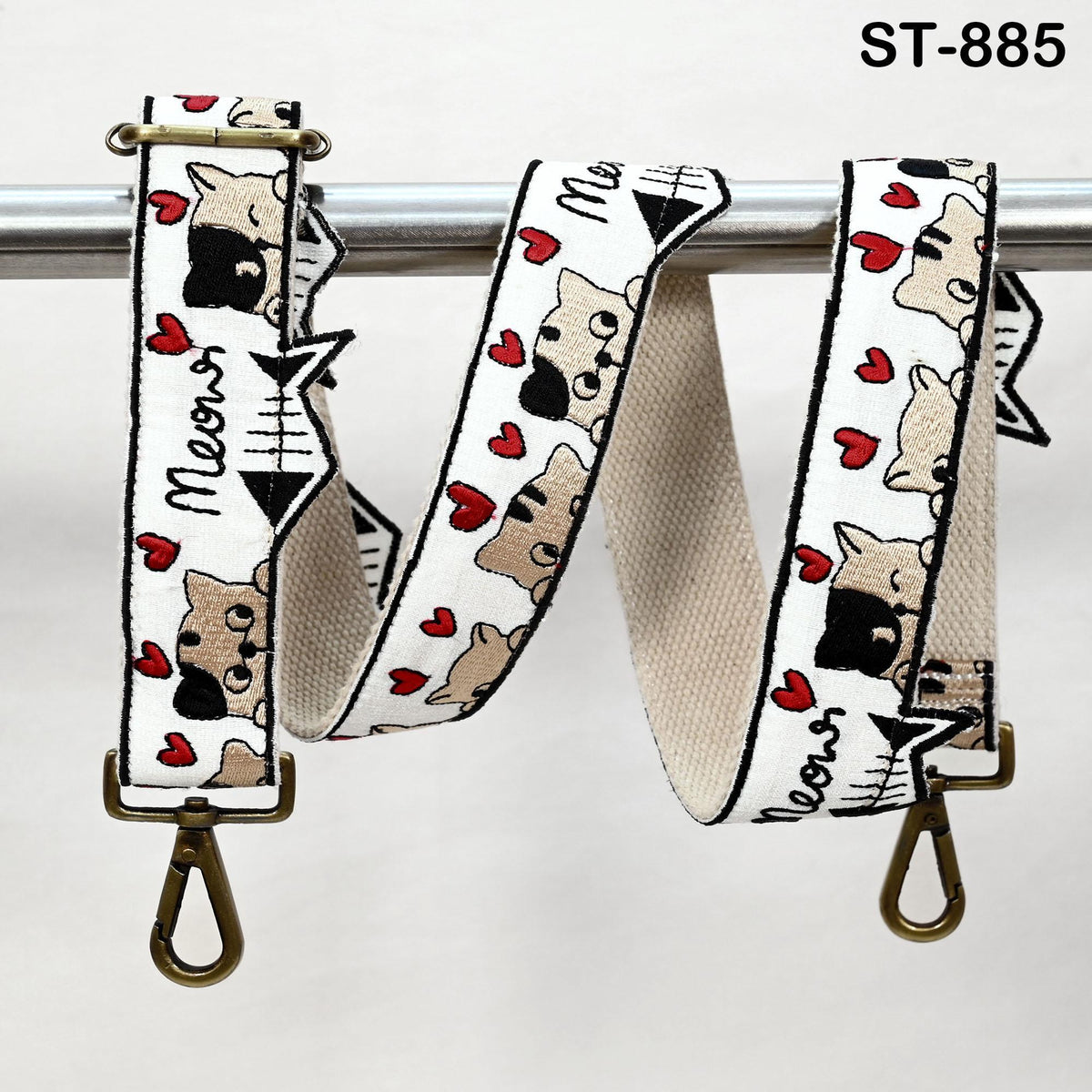 A strap with a cat design printed on it, featuring a repeating pattern of cats and hearts. The strap is hanging on a metal bar, and there are two metal hooks attached to it.