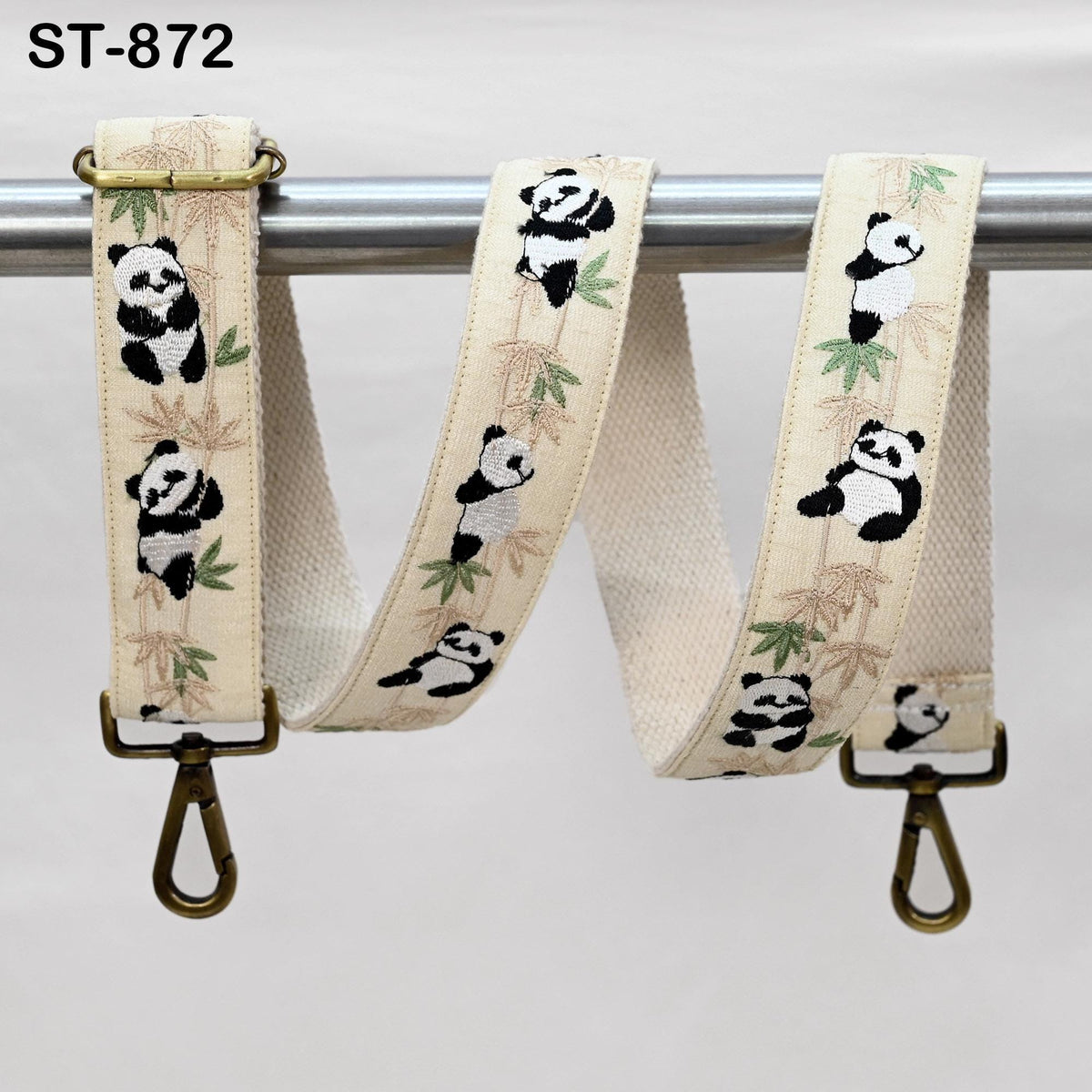 A beige strap with a panda bear design printed on it, hanging from a metal bar.