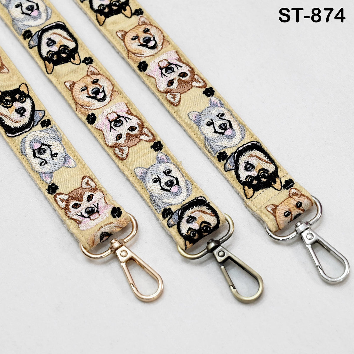 a beige strap with a repeating pattern of dog faces, including Shiba Inu, a breed of dog. The strap has three metal hooks at the ends, which are designed to attach to bags or straps.
