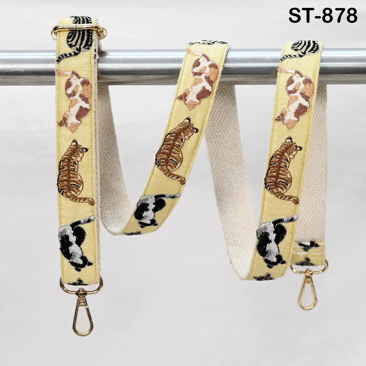 a beige strap with a repeating pattern of cats and stripes, hanging on a metal bar.
