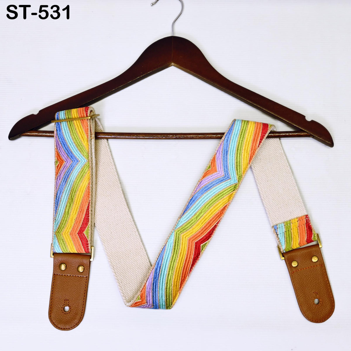 A colorful, patterned guitar strap is hanging on a wooden hanger against a white background.