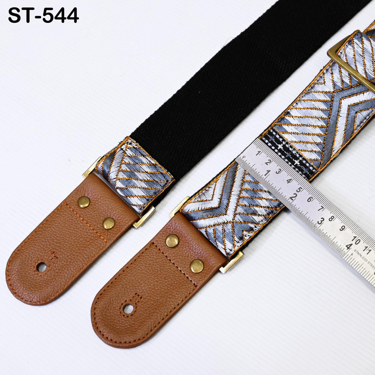 A close-up image of a guitar strap with a black and white patterned design, placed next to a ruler for size comparison.